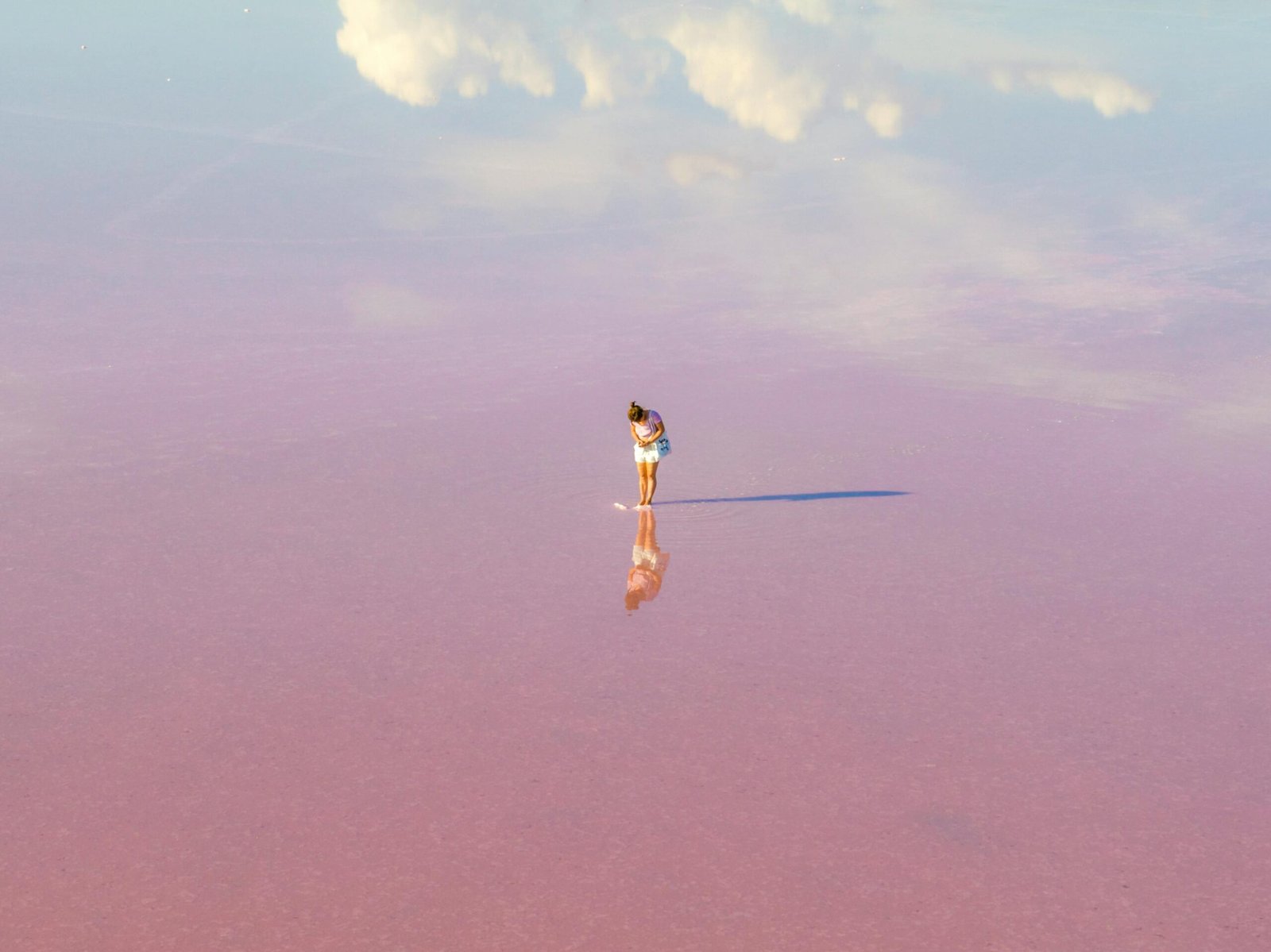 A woman stands on a vast pink salt lake, reflecting clouds in Dimboola, Australia.